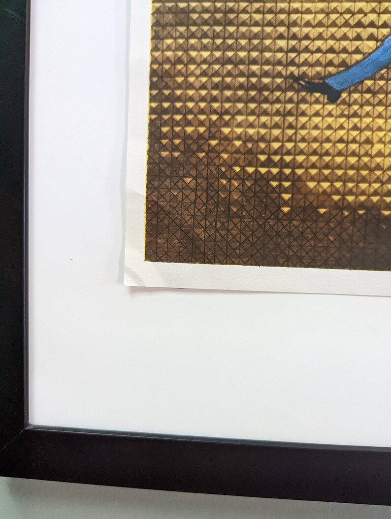 May include: A framed print with a black frame. The print features a geometric pattern in shades of brown and gold, with a blue element. The print is mounted on a white mat.