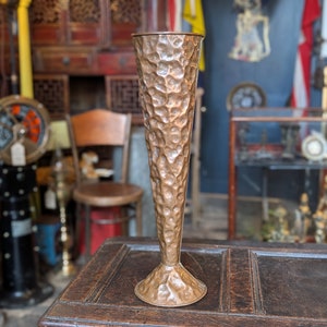 Könnte beinhalten: Eine gehämmerte Kupfervase mit einer hohen, konischen Form. Die Vase hat eine strukturierte Oberfläche und einen breiten Boden.