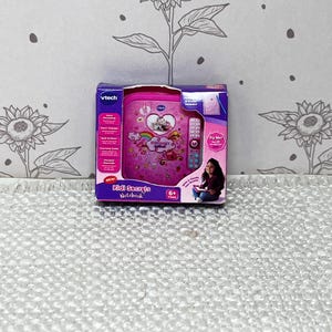 May include: A pink VTech Kidi Secrets Notebook in its original packaging. The notebook features a heart, rainbow, and cloud design. The packaging includes the text "Kidi Secrets Notebook" and "6+ Years".
