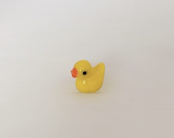 May include: A small yellow rubber duck with a black eye and an orange beak.