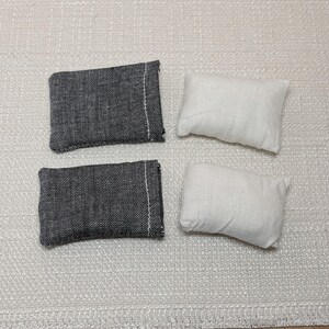 May include: Four small rectangular cushions. Two are dark grey with a white seam, and two are white. The cushions are arranged on a textured, off-white rug.