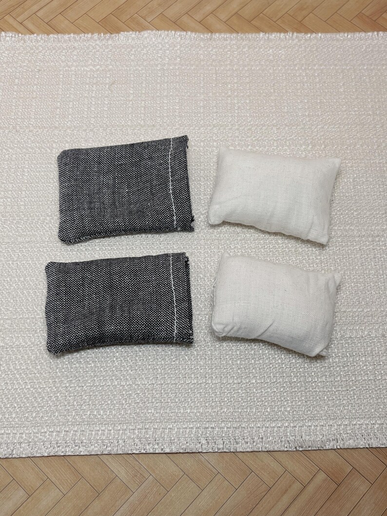May include: Four small rectangular cushions. Two are dark grey with a white seam, and two are white. The cushions are arranged on a textured, off-white rug.