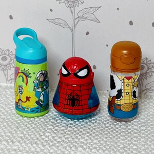May include: Three character-themed bottles. A green and blue water bottle with Toy Story characters, a red and blue Spider-Man bottle, and a Woody-themed bottle with a brown lid.