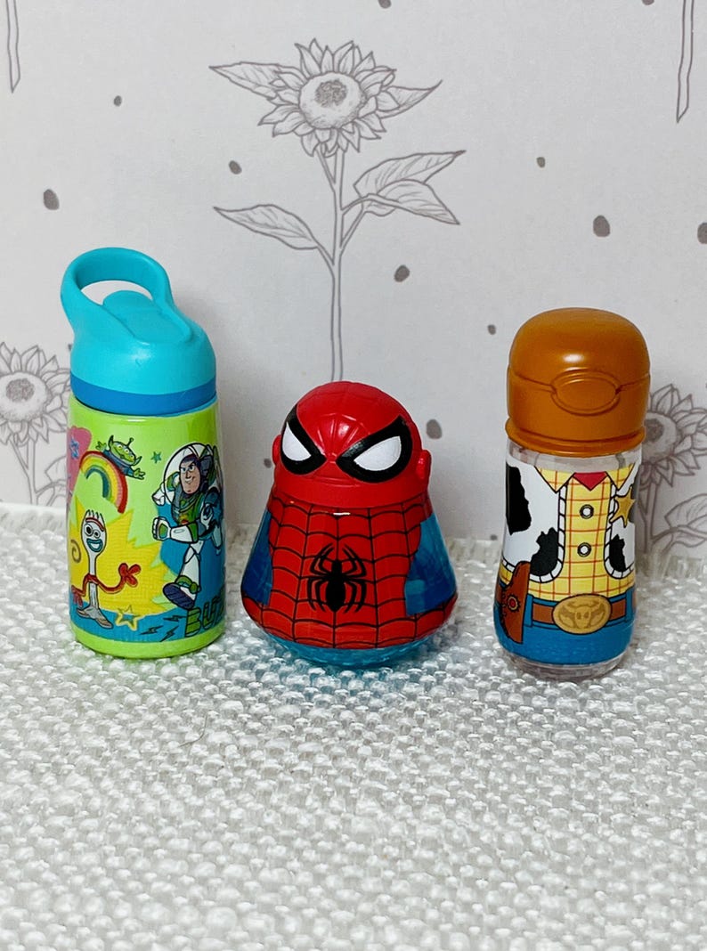 May include: Three character-themed bottles. A green and blue water bottle with Toy Story characters, a red and blue Spider-Man bottle, and a Woody-themed bottle with a brown lid.