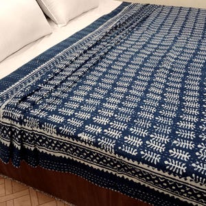 Può includere: Una trapunta a motivi blu navy e bianchi copre un letto, con due cuscini bianchi visibili. La trapunta presenta un motivo a forma di foglia ripetuto e un bordo decorativo. Il copriletto è realizzato in materiale morbido.