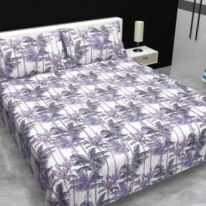 May include: A bed covered with a white sheet and pillowcases featuring a repeating pattern of purple palm trees. The bedding set includes two pillowcases and a fitted sheet. The room has a white headboard and a side table with a lamp.