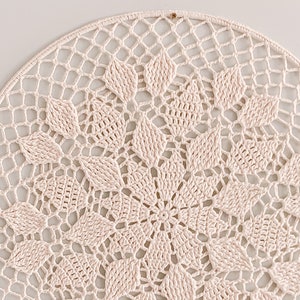 Op de afbeelding: Een wit gehaakt doily met een delicaat bloemenpatroon. De doily is rond en heeft een kantpatroon.