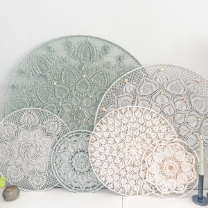 May include: A set of five decorative wall hangings in various sizes. The hangings are made of a delicate, lacy material in shades of white and light green. They feature intricate patterns and designs, resembling crocheted doilies.