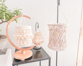 May include: Three crocheted hanging lamps with wooden beads. The lamps are made of natural cream colored yarn and are hanging from a wooden stand and a black metal stand.