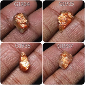 May include: Four sunstone gemstones, each with a unique shape and color variation, ranging from orange to red with a shimmery, iridescent effect. The stones are labeled G1934, G1935, G1936, and G1937.