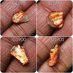 May include: Four pieces of sunstone, each with a different shape and size. The sunstone is a reddish-orange color with a shimmery, iridescent effect. The stones are labeled with the codes G1898, G1899, G1900, and G1901.