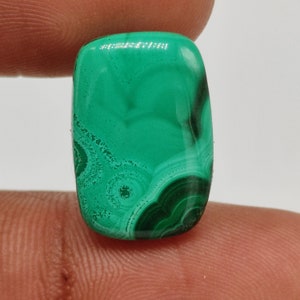 Peut inclure: Un cabochon de malachite verte avec un motif tourbillonnant. La pierre est taillée en forme rectangulaire et a une surface lisse et polie.