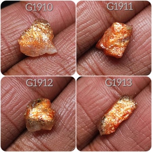 May include: Four pieces of raw, rough, orange and gold sunstone crystals with iridescent shimmer. The crystals are labeled G1910, G1911, G1912, and G1913.