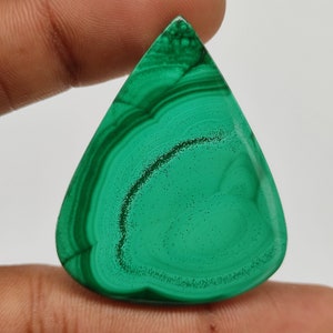 Peut inclure: Un cabochon de malachite verte en forme de larme. La pierre présente un motif tourbillonnant de vert foncé et clair.