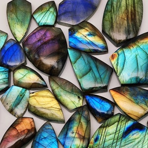 May include: A collection of iridescent labradorite gemstone cabochons in various shades of blue, green, and gold. The stones are cut in a teardrop shape and have a smooth, polished finish.