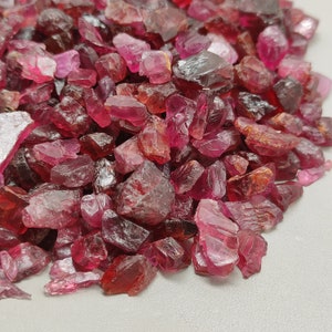 May include: A pile of loose, faceted, red ruby gemstones. The rubies are various sizes and shapes, with some having a more pink hue.