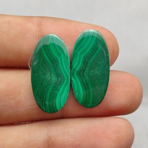 Peut inclure: Deux cabochons ovales en malachite verte avec un motif tourbillonnant. Les pierres sont lisses et polies.