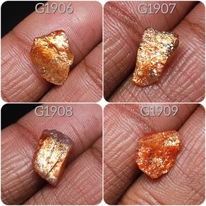 May include: Four rough, raw, orange and gold sunstone crystals with iridescent sparkle. The crystals are labeled G1906, G1907, G1908, and G1909.
