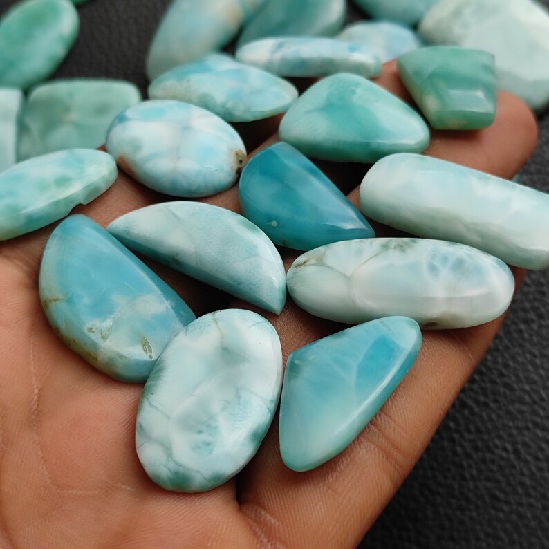 May include: A collection of blue and white gemstone cabochons, some oval, some half-moon shaped, and some triangular. The stones have a cloudy, marbled appearance.