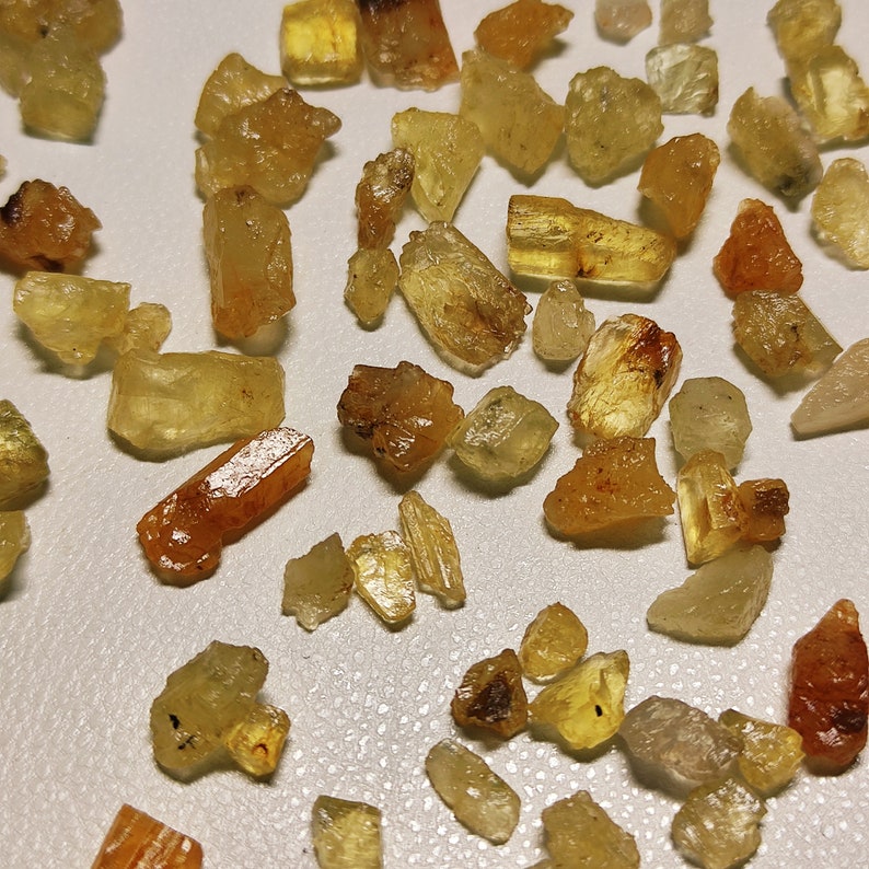 May include: A collection of small, translucent, yellow-brown crystals. The crystals are of various shapes and sizes, and some have a more orange hue.