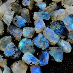 May include: A collection of iridescent blue and white moonstone rough stones. The stones are various sizes and shapes, with a natural, raw finish.