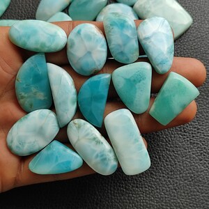 May include: A collection of 15 blue and white gemstone cabochons, with a variety of shapes and sizes. The cabochons are smooth and polished, with a cloudy, marbled appearance.