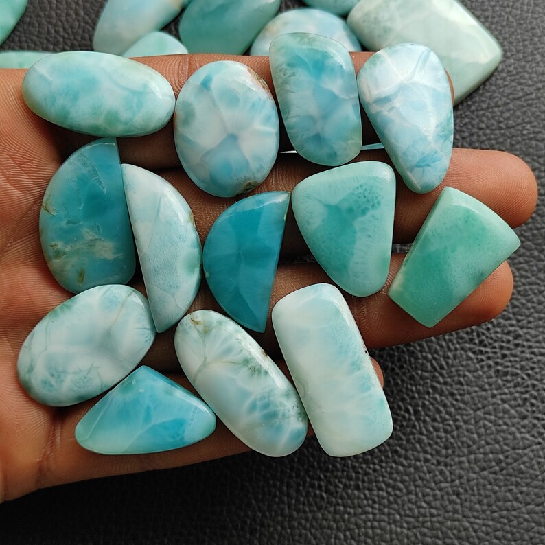 May include: A collection of 15 blue and white gemstone cabochons, with a variety of shapes and sizes. The cabochons are smooth and polished, with a cloudy, marbled appearance.