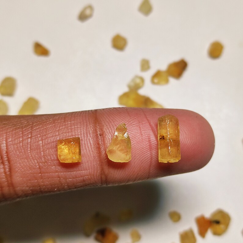 May include: Three yellow-brown gemstones of varying sizes and shapes. The gemstones are held on a finger.
