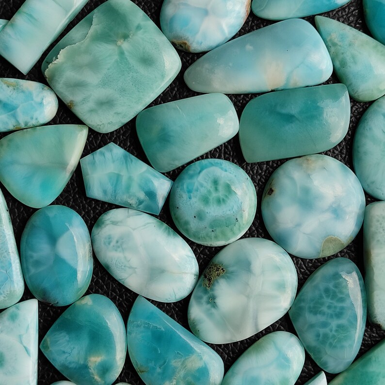 May include: A collection of various sizes and shapes of blue and green gemstone cabochons. The stones have a cloudy, marbled appearance.