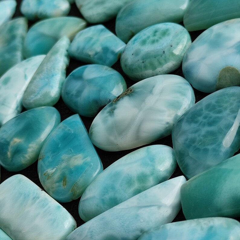 May include: A collection of polished blue and white ocean jasper stones. The stones are smooth and have a variety of shapes and sizes.
