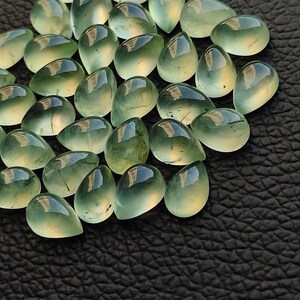 May include: A collection of green gemstone cabochons in a teardrop shape. The stones are translucent and have a slight shimmer.
