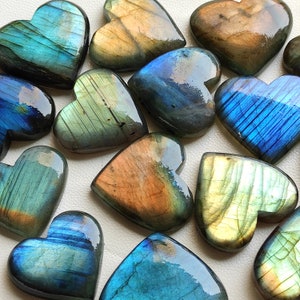 May include: A collection of heart-shaped labradorite stones in shades of blue, green, and gold. The stones are polished and have an iridescent sheen.