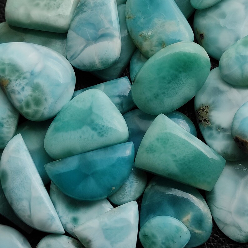 May include: A collection of various shapes and sizes of blue and green gemstone cabochons. The cabochons have a cloudy, marbled appearance.