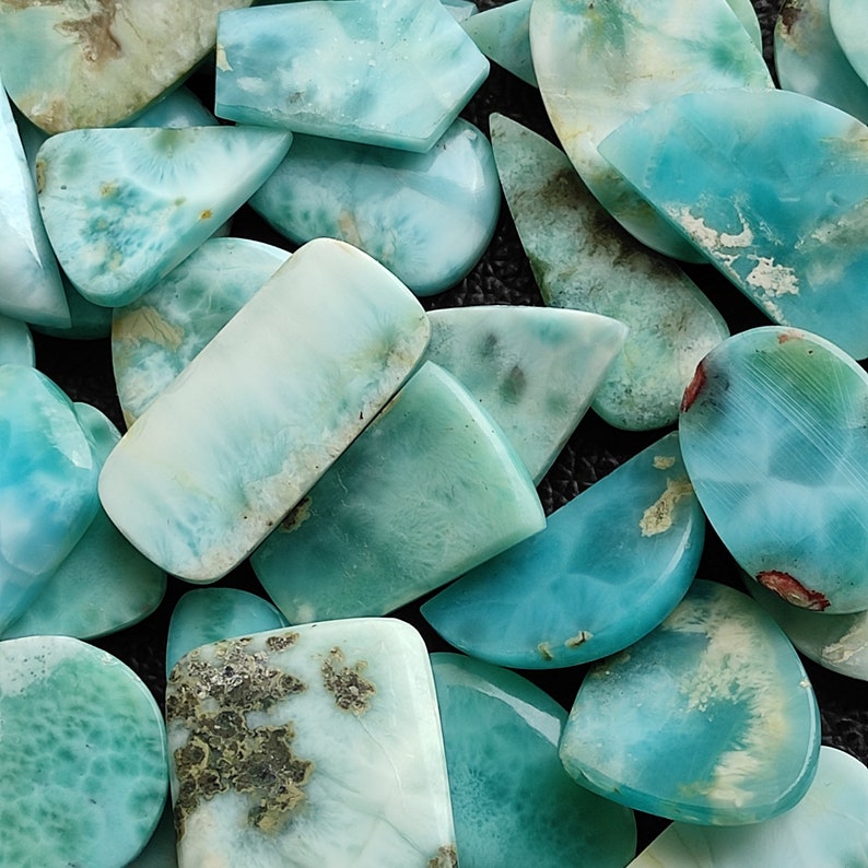 May include: A collection of light blue and green gemstone cabochons with a variety of shapes and sizes. The cabochons have a cloudy, marbled appearance.