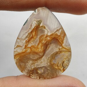 Peut inclure: Un cabochon d'agate en forme de larme avec un motif de couleur blanc, brun et vert. L'agate a une apparence translucide avec un motif tourbillonnant de dendrites brunes.