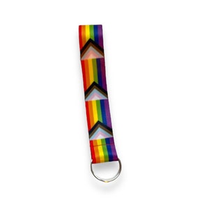 May include: A rainbow-coloured key chain with a silver key ring. The rainbow is made up of six stripes with a black and white chevron pattern.