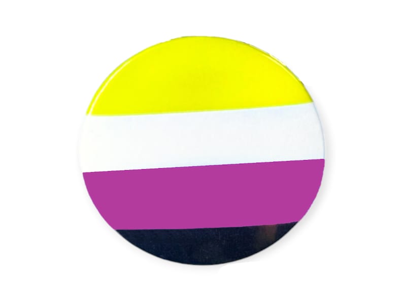 以下が含まれることがあります： 黄色、白、紫、黒のストライプ模様の丸いボタン。このボタンはノンバイナリープライドフラッグを表しています。