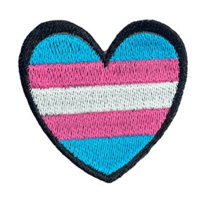 Pode incluir: Um remendo bordado em forma de coração com as cores da bandeira do orgulho transgénero: azul claro, rosa e branco.