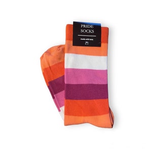 Könnte beinhalten: Ein Paar gestreifte Socken in den Farben der lesbischen Pride-Flagge: Orange, Rosa, Weiß und Lila. Die Socken sind gefaltet und haben ein Etikett mit der Aufschrift "PRIDE SOCKS made with love 36-41".