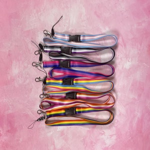 Peut inclure: Un ensemble de huit lanières colorées avec différents motifs de drapeaux arc-en-ciel. Les lanières sont en tissu tissé et ont un clip en plastique noir à l'extrémité.