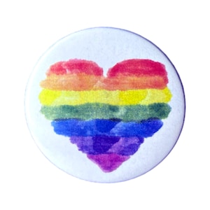 Può includere: Un bottone rotondo bianco con un cuore arcobaleno dipinto su di esso. Il cuore è composto da sei colori: rosso, arancione, giallo, verde, blu e viola.