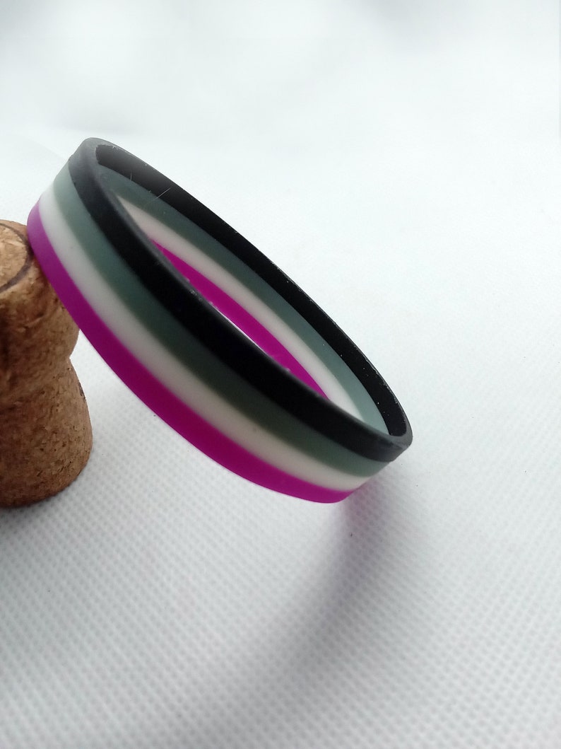 May include: A black, white, gray, and purple silicone bracelet. The bracelet is a symbol of the asexual pride flag.