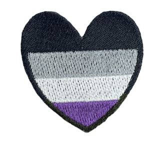 Może przedstawiać: Naszywka w kształcie serca z kolorami flagi dumy aseksualnej: czarny, szary, biały i fioletowy.
