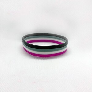 May include: A purple, white, black, and gray silicone bracelet with five stripes.