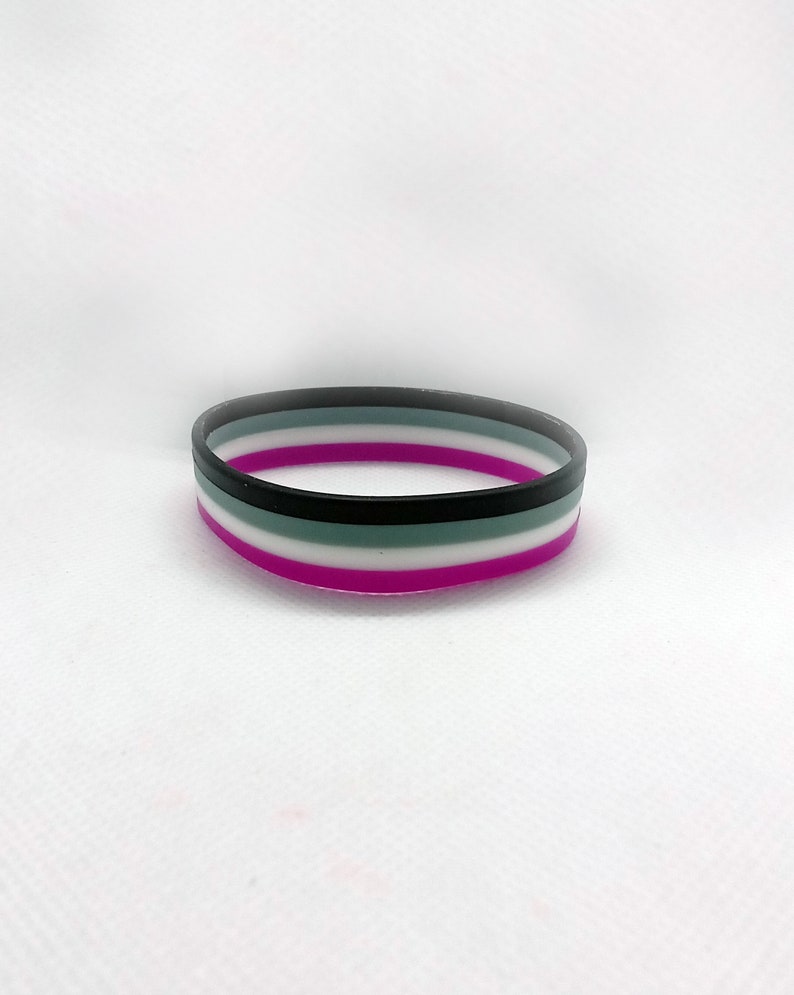 May include: A purple, white, black, and gray silicone bracelet with five stripes.