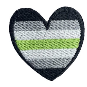 May include: Embroidered heart patch displaying the aromantic pride flag. The design features horizontal stripes in black, grey, white, and green, with a black border. This patch can be ironed on or sewn onto fabric.