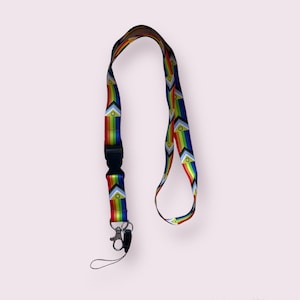 Op de afbeelding: Een regenboog-koord met een zwarte clip en een zilveren draaibare haak. Het koord heeft een herhalend patroon van regenboog-driehoeken met een gele cirkel in het midden.