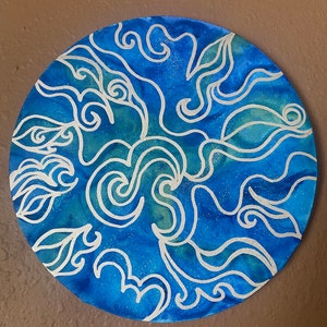 Pu&ograve; includere: Una tela rotonda dipinta di blu e bianco con un design astratto a spirale. Il design ricorda le onde o le nuvole.