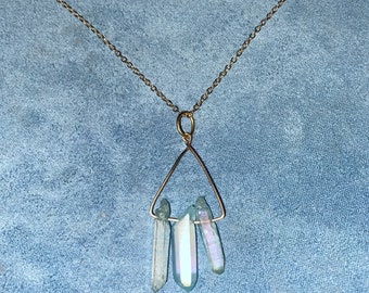 Può includere: Una collana con catena dorata con un ciondolo triangolare che tiene tre punte di cristallo blu iridescente.