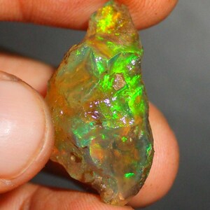 Puede incluir: Una piedra preciosa de ópalo en bruto, de color verde y naranja, con destellos iridiscentes.